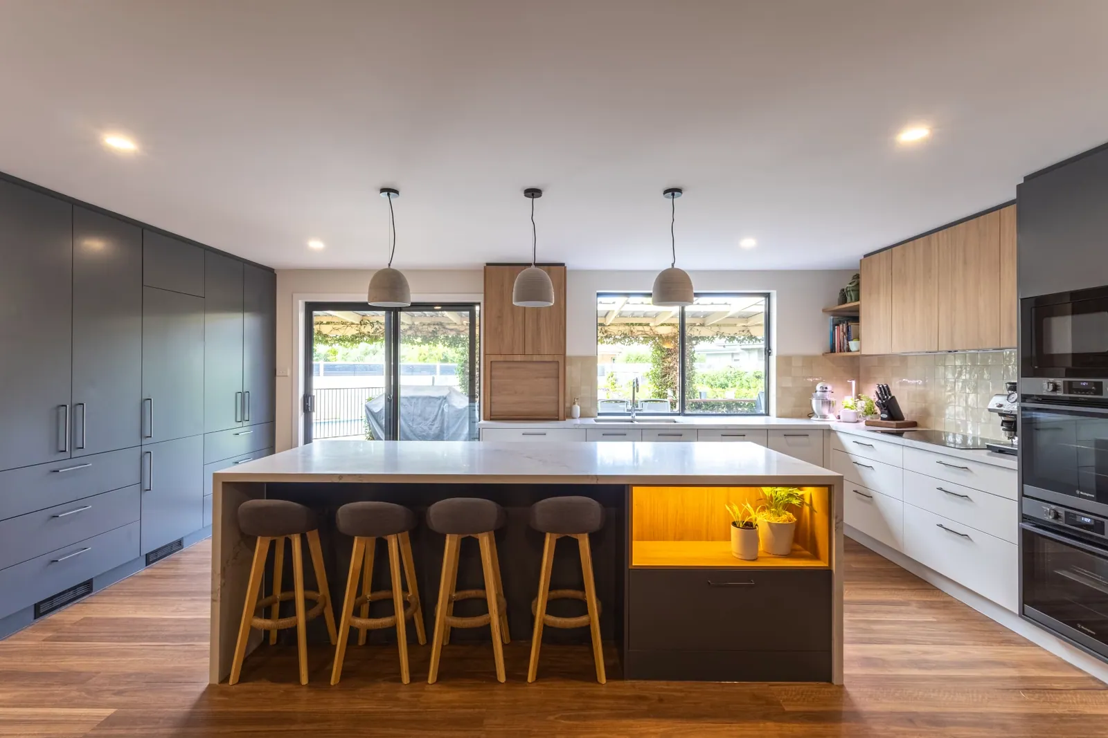 Kaleen island with seating, pendant lighting and dark grey cabinetry behind