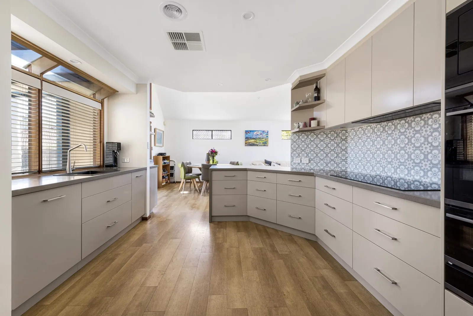 Nicholls galley kitchen with light cabinetry, a patterned splashback and timber-look flooring